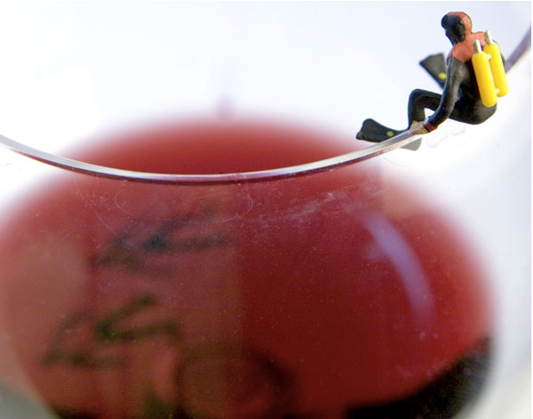 A scuba diver sits on the edge of a wine glass.